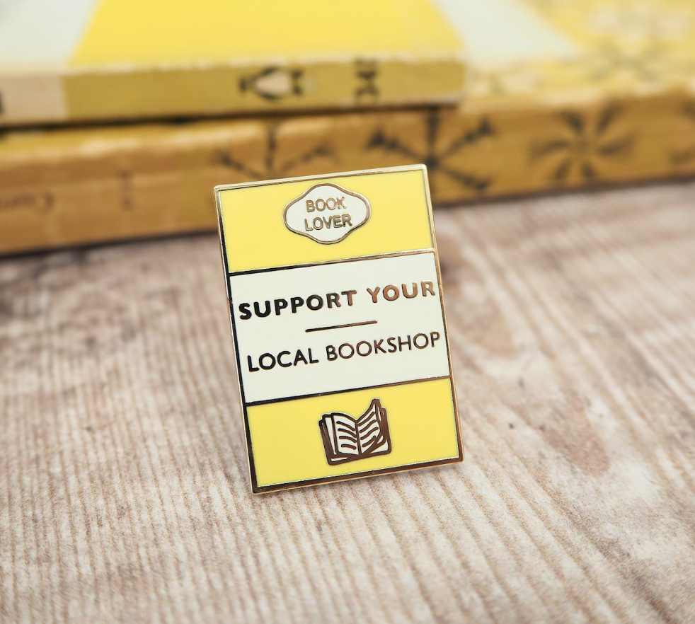 Image of a yellow and white enamel pin designed to look like a Penguin Classics book that says "support your local bookshop"