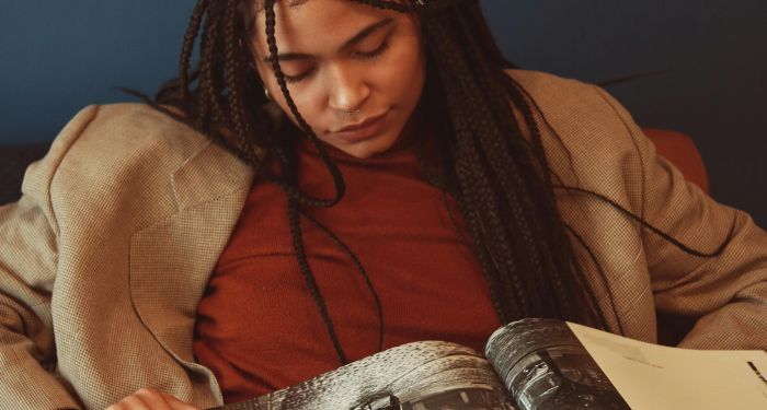 a light brown-skinned Black woman with braids and a jacket reading