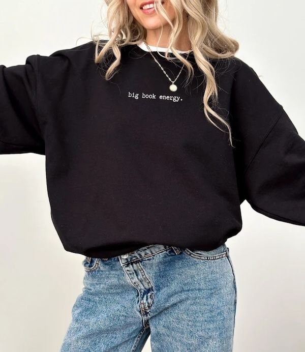 black crewneck sweater with small white text on the front that reads "big book energy"