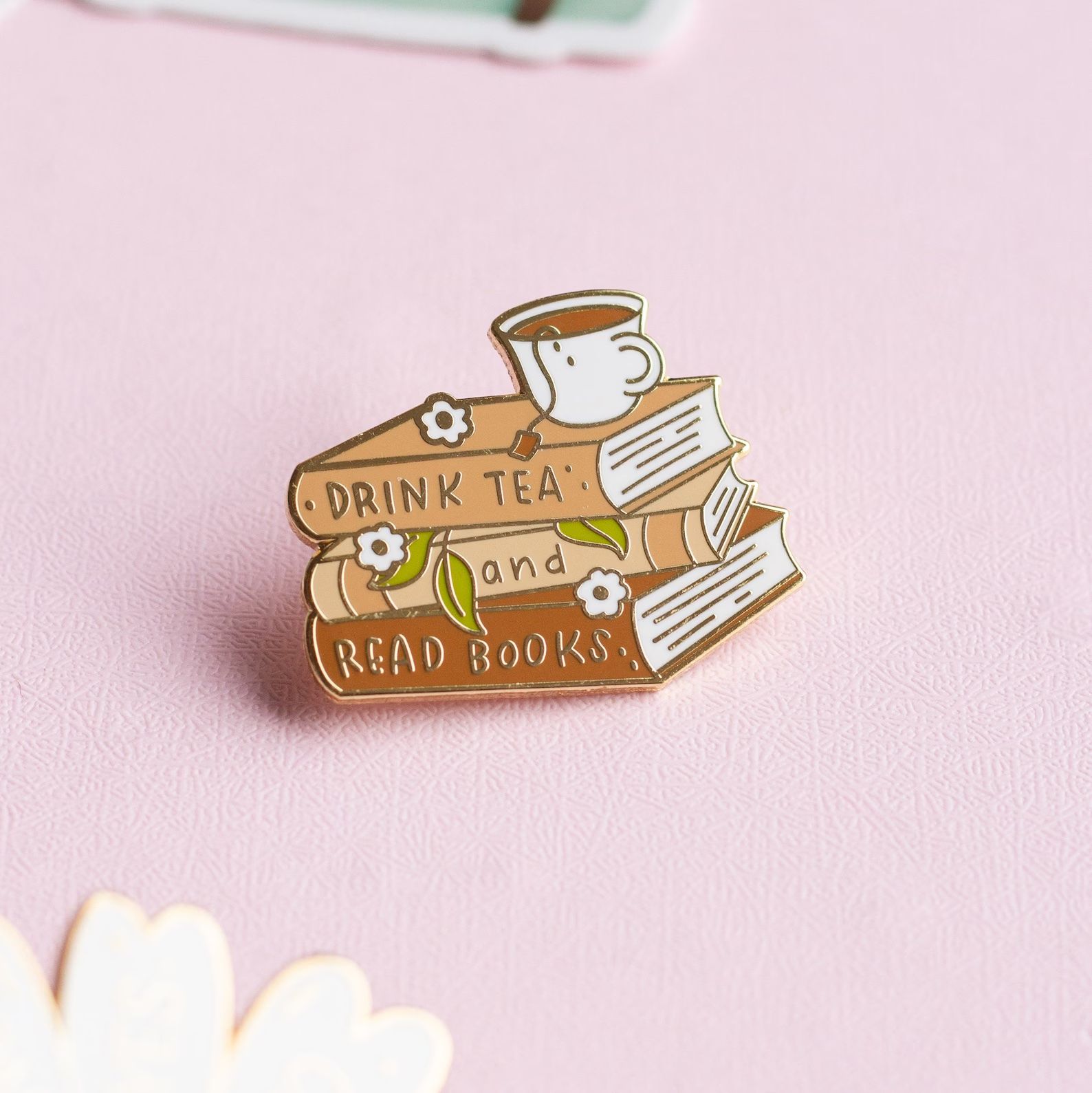 a photo of an enamel pin that reads "Drink Tea and Read Books"