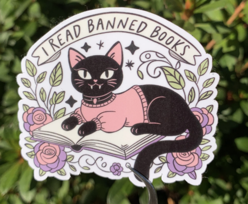 I read banned books sticker; image of black cat in a pink sweater sitting on an open book