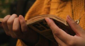 a medium light skinned hand holding a book; the person is wearing a yellow sweater