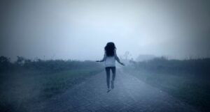 a dark-haired woman levitating on a foggy road