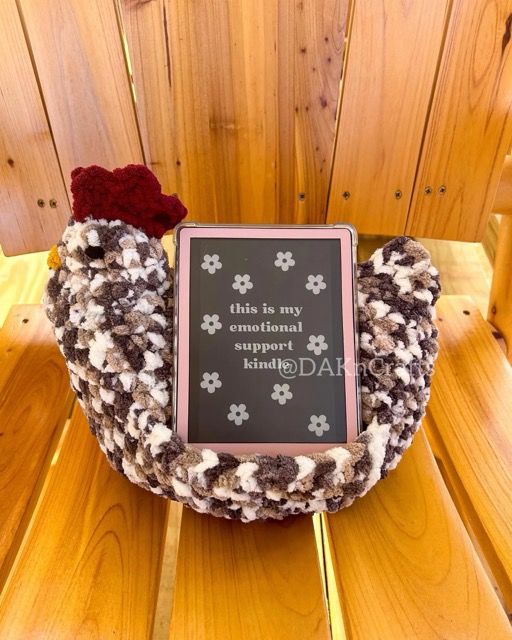 Crochet chicken sitting on a wooden chair with an ereader.