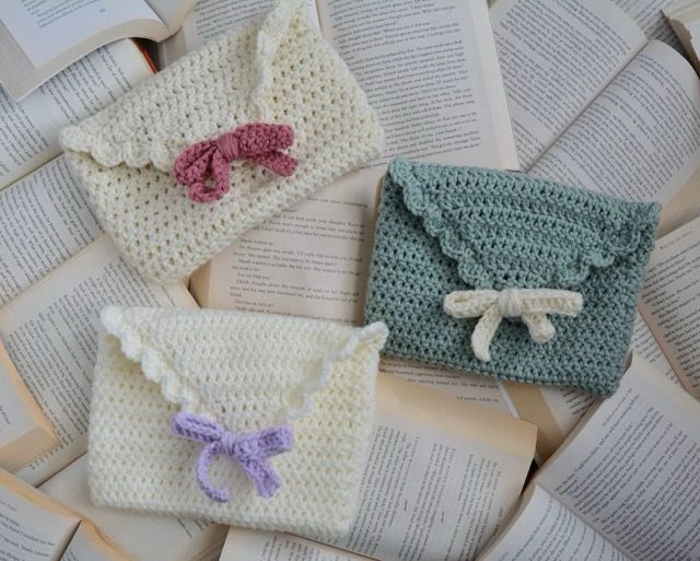 Crochet bow Love letter book sleeve in white and red, white and purple, and green in white on a pile of open books.