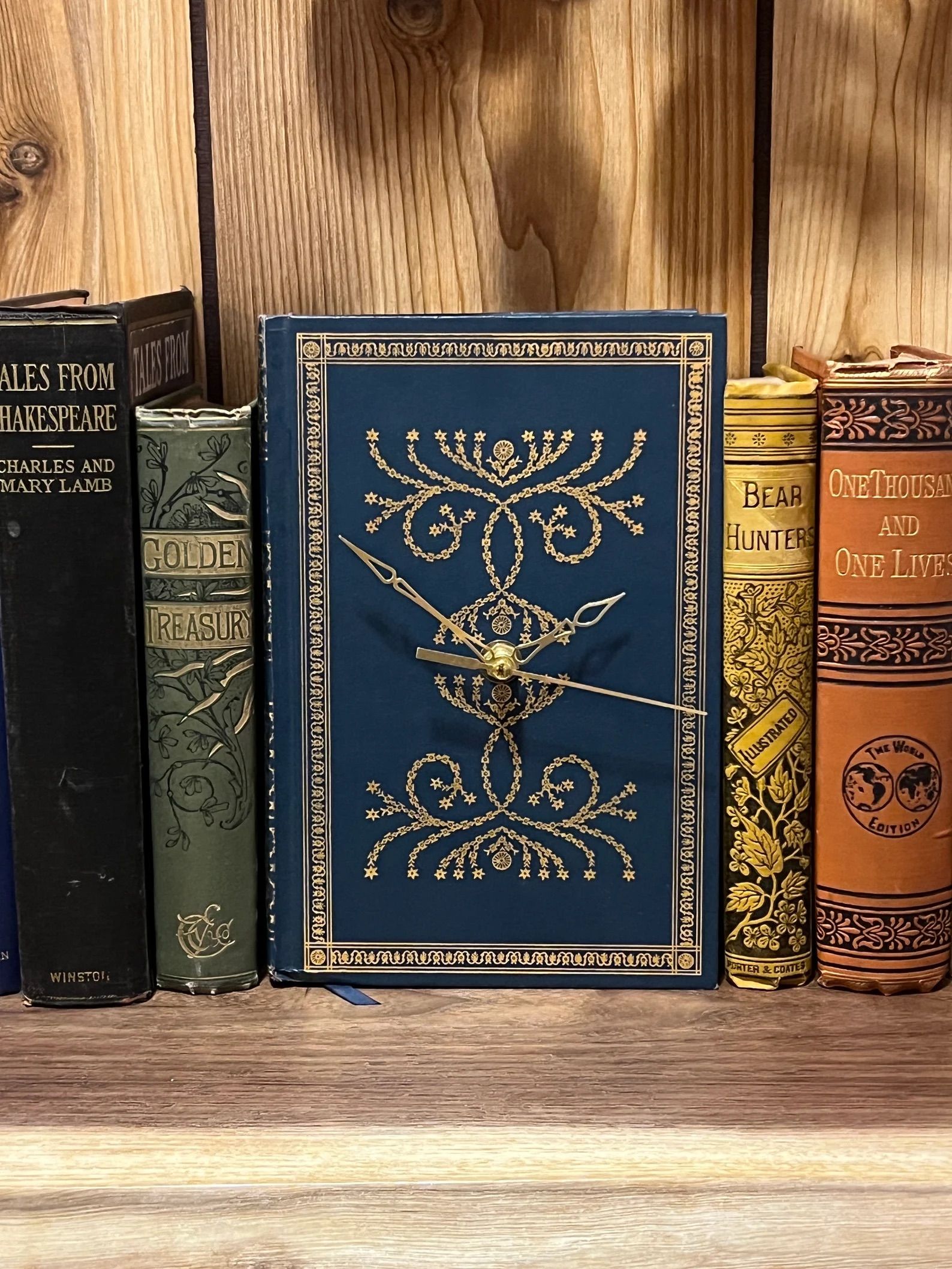 Blue hardcover book with a clock in front of wood wall next to other old books.