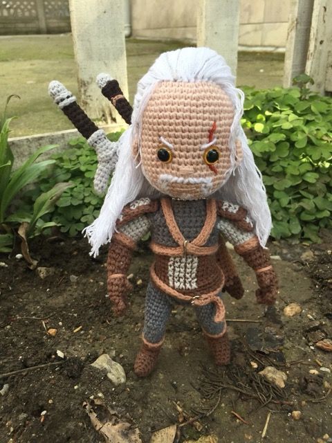 The Witcher Crochet doll in a yard with a railing. 