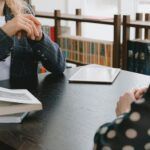 two people talking at a table with books between them