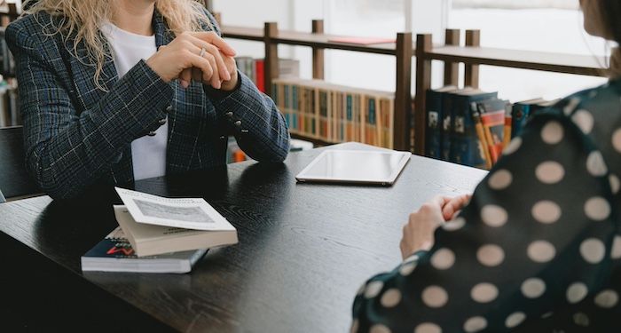 two people talking at a table with books between them