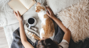 a person petting a cat while reading in bed