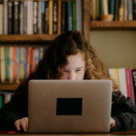 a young teen working on a laptop with bookshelves in the background