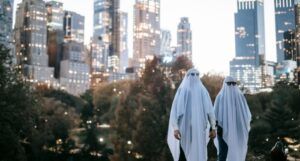 a couple holding hands in a city wearing white sheets over their heads to look like ghosts