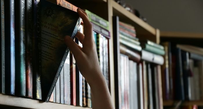 image of a hand pulling a book off a library shelf