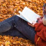 a child reading a book in a pile of leaves while leaning against a tree