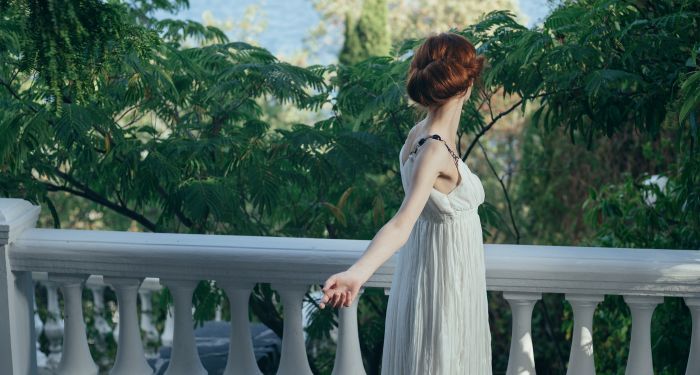 a white woman in a white empire waist dress gazing out at trees