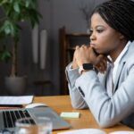 a Black woman in a suit resting her chin on her hands and staring at a laptop screen