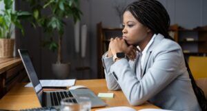 a Black woman in a suit resting her chin on her hands and staring at a laptop screen