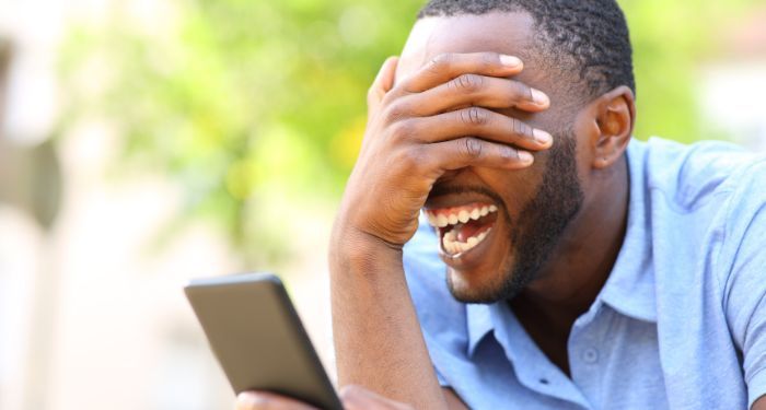 a Black man covering his eyes and laughing with an ereader in the other hand