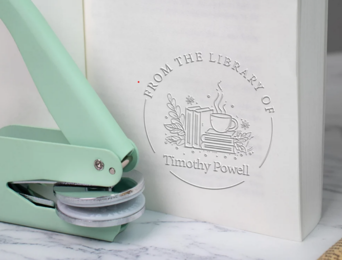 A metal embosser beside a piece of paper embossed with a "from the library of' message