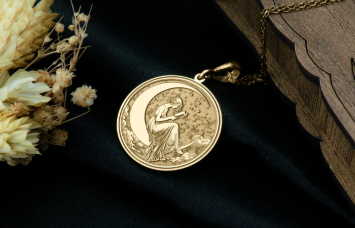 A golden pendant with a design of a woman reading and sitting on a crescent moon