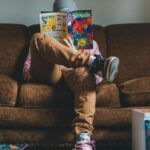 Young man sitting on sofa and reading comics magazine