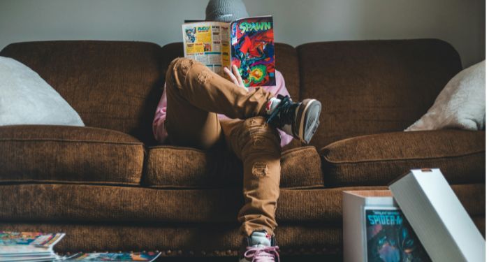 Young man sitting on sofa and reading comics magazine