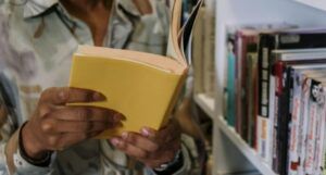 a brown-skinned person holding a book with a yellow cover