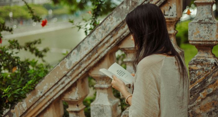 a fair-skinned woman reading on antique steps