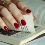 fair-skinned hand with red nail polish turns a page in a book