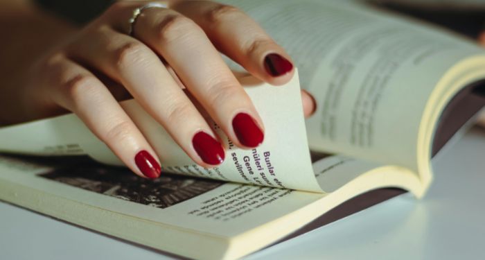 fair-skinned hand with red nail polish turns a page in a book