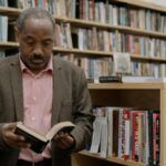 older, brown-skinned Black man reading in a library