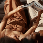 a photo of a Black queer couple reading together, holding the book above them