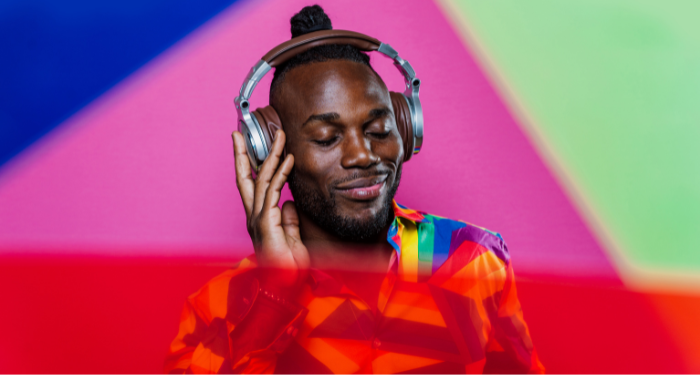 a Black person wearing a rainbow shirt listening to headphones