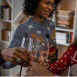 three Black people of varying skin tones smiling and clinking champagne glasses during the holidays