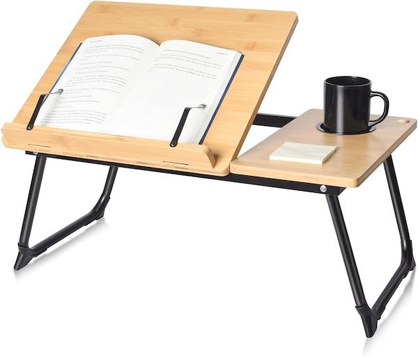 bamboo laptop stand with black hardware. an open book is resting on one side, a black mug and stack of sticky notes is on the other