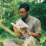 tan-skinned Asian man reading a book while sitting outside