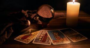 four tarot cards fanned out in front of a crystal ball and a lit candle on a wood surface in a dark room