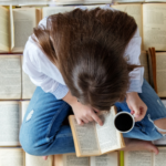 a young person with light skin and long brown hair reads on a floor of open books