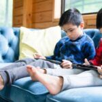 two little boys sitting on a blue couch. Both children are on digital devices