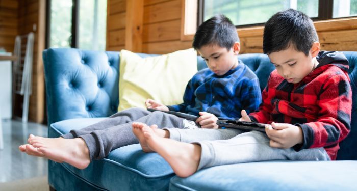 two little boys sitting on a blue couch. Both children are on digital devices