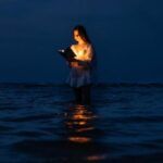 a fair-skinned young woman reading an illuminated book in the ocean