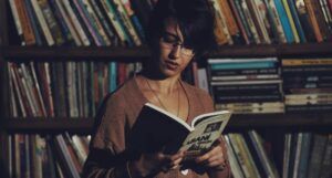 a tan-skinned woman with dark hair reading a book i a used book store