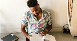 brown-skinned black man sitting on floor and reading, books surround him