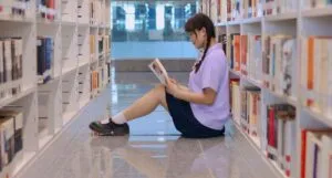 fair skinned Asian woman sitting in a library aisle reading