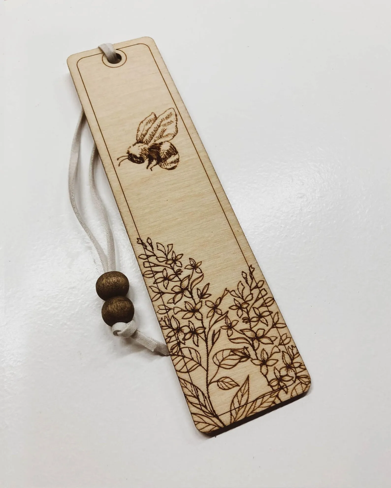 a wooden bookmark with an illustration of a honeybee and lilac flowers