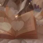 overlay of glowing hearts on image of books opened on bed and string lights